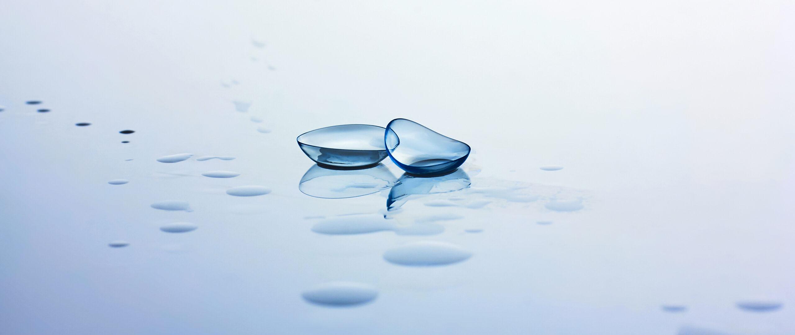 Contact lenses and water drops on light blue background